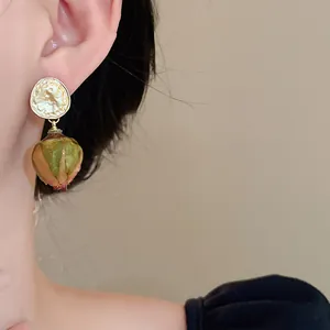 Dettaglio di orecchini dorati martellati con bocciolo di rosa stabilizzato su modella.