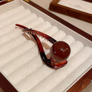 Close-up of elegant amber resin duckbill clip with round bead in a velvet box.