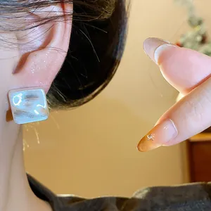 Primo piano di orecchini a lobo quadrati minimalisti in argento con finitura spazzolata