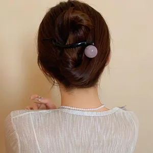 Close-up view of a minimalist black resin duckbill hair clip with a pink sphere ornament.