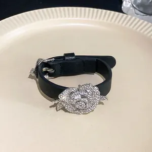 Detail view of a black leather strap bracelet with a sparkling rhinestone rose charm.