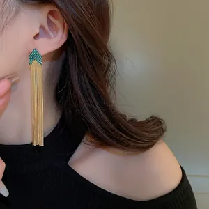 Dettaglio di eleganti orecchini a nappa dorati con design a freccia in strass verdi