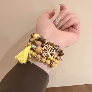 Detailed view of a bohemian multi-layer beaded bracelet with yellow tassel and tree charm