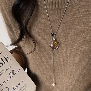 Detailed view of fashionable rocking horse necklace with pearl on brown knit sweater