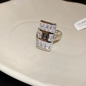 Close-up of square zircon ring featuring a central S logo and chain band