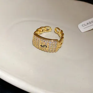 Macro detail of a gold chain ring featuring a zircon-encrusted square face and open band.