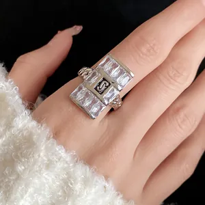 Close-up of a luxury square zircon ring with a chain band and center logo on a hand.