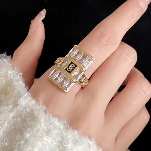 Close-up of gold-colored square zircon ring with a stylized monogram logo