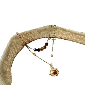 Vintage gold necklace with tiger eye beads and sun-shaped pendant on white background