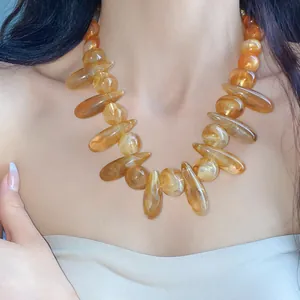 Close-up of a chunky amber acrylic swirl necklace with irregular beads on model neck