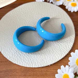 Vibrant blue acrylic C-shaped stud earrings presented on a textured leather display pad.