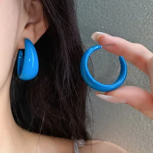 Detailed close-up of vibrant blue acrylic C-shaped earrings shown on ear and held