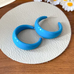 Detail view of bold blue acrylic C-shape hoop earrings on a textured display pad