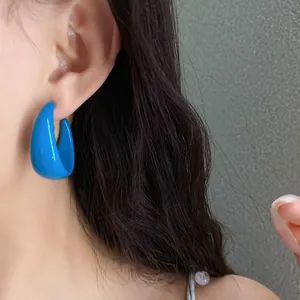 Close-up view of bright blue C-shaped acrylic earrings showing elegant fit on the ear.