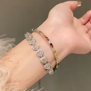 Close-up of heart-shaped pink zircon bracelet and colorful gemstone bangle on wrist