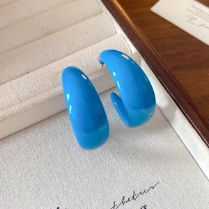 Close-up of vibrant blue acrylic C-shaped hoop earrings in a cream jewelry box