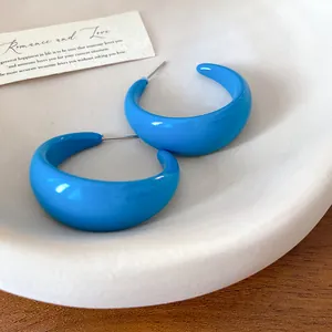 Detailed view of bold blue C-shaped acrylic hoop earrings placed on a minimalist dish