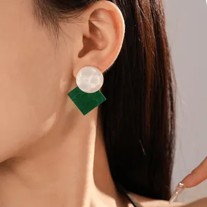 Close-up of shimmering green and white geometric resin stud earrings worn on ear