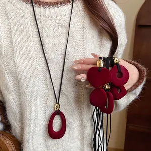 Close-up view of red flocked heart and oval pendant necklaces on a cream cable knit sweater