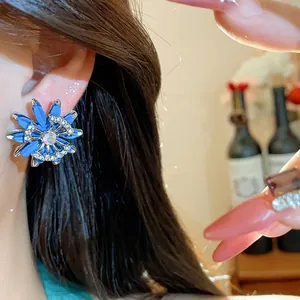 Close-up detail of a vintage blue flower earring with crystals on an Asian model's ear.