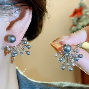 Dettaglio di orecchini eleganti con zirconi e perle a forma di fuochi d'artificio sul lobo.