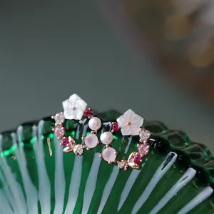 Dettaglio di orecchini floreali con petali di conchiglia e perle su base in vetro verde
