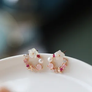 Dettaglio di orecchini a ghirlanda floreale con perle e cristalli su un piatto bianco.