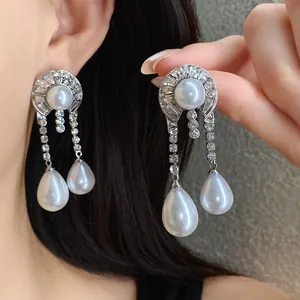 Primo piano di orecchini vintage in argento con perle a goccia e cristalli scintillanti.