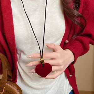 Detail view of a vintage red flocked heart pendant necklace worn with a red cardigan