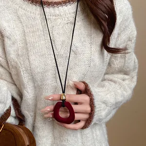 Close-up of a vintage red flocked pendant necklace held by a woman in a beige sweater.