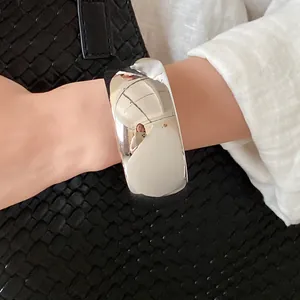 Close-up of minimalist glossy silver open bangle on wrist with woven bag background.