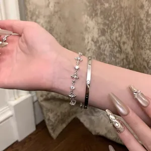 Close-up of zircon fleur-de-lis cross bracelet and minimalist screw bangle on wrist