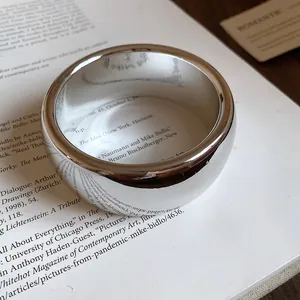 Macro view of a glossy minimalist silver-finish open bangle bracelet on an open book.