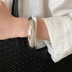 Detail shot of a chunky polished silver-colored minimalist bangle on a model's wrist.