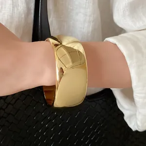 Close-up detail of a minimalist glossy gold twisted open cuff bracelet on a model's wrist