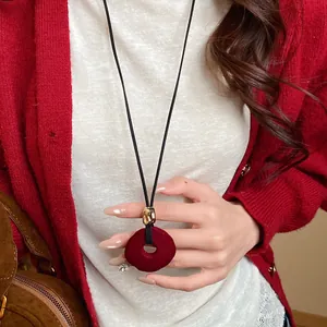 Close-up of a red flocked circular pendant necklace held by a woman in a red cardigan