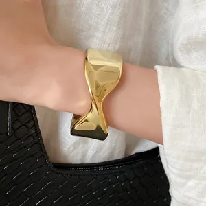 Close-up detail of a minimalist gold twisted open cuff bracelet worn on a woman's wrist