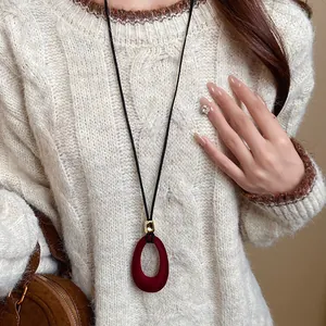 Detailed view of a red flocked oval pendant necklace on a cozy white cable-knit sweater.