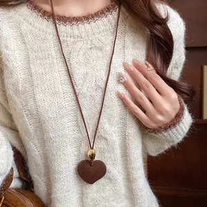 Detailed view of brown flocked heart pendant necklace worn over a cozy beige knit sweater