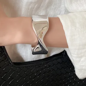 Close-up detail of a minimalist silver glossy twisted open cuff bracelet on wrist