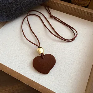 Detail of dark brown flocked heart pendant necklace with gold bead on suede cord