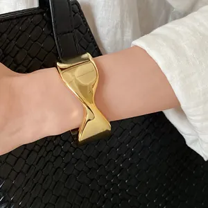 Detailed close-up view of a glossy gold twisted open cuff bracelet on a woman's wrist