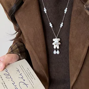 Gros plan d'un collier ours blanc avec des perles porté sur des vêtements d'hiver bruns.