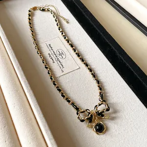 Détail d'un collier chaîne dorée entrelacée de similicuir avec un élégant pendentif nœud