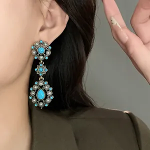 Close-up of vintage flower and teardrop earrings with turquoise stones and pearls on a model.