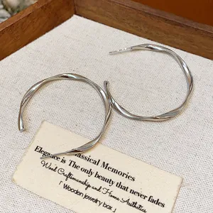 Macro detail of minimalist silver twisted hoop earrings in a wooden jewelry box.