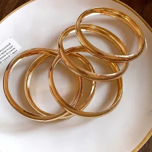 Minimalistische goldglänzende runde Armreifen auf einem dekorativen weißen Porzellanteller