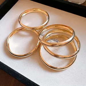 Set aus fünf minimalistischen, goldfarbenen, glatten runden Armreifen in einer Schmuckschale