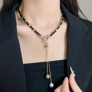 Détail d'un collier chaîne dorée et cuir noir avec un pendentif en perle.