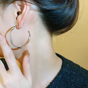 Close-up detail view of a minimalist silver twisted hoop earring on an Asian model's ear